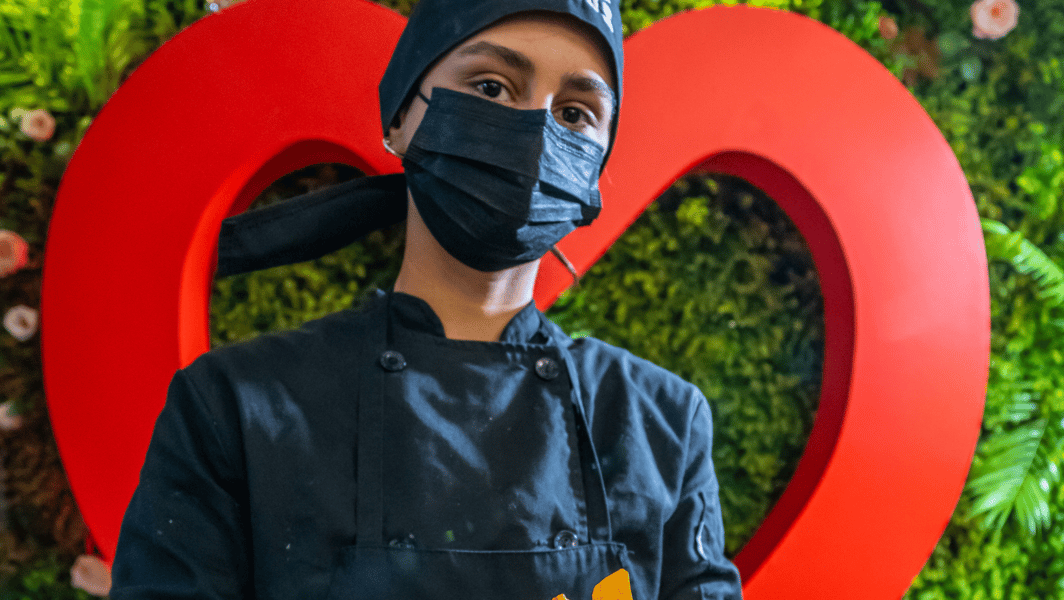 camarera posando delante de la decoración de un restaurante, con un cartel en forma de corazón. 